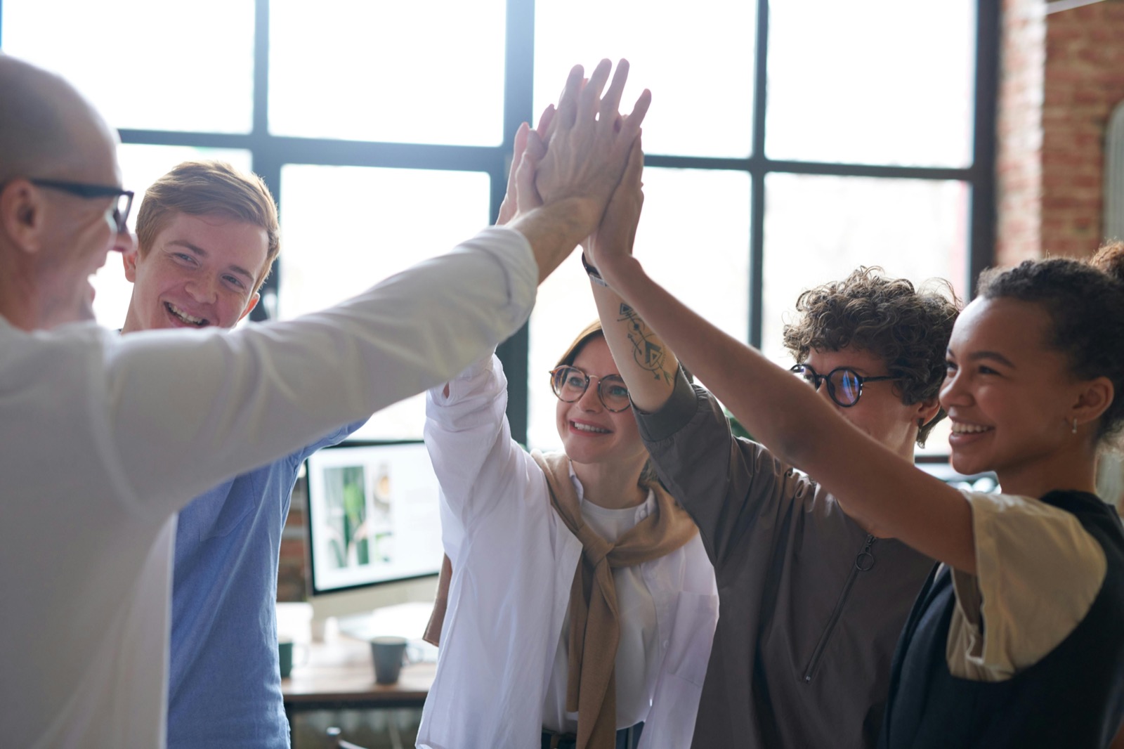 A group of people celebrating together with a high-five in a sunlit room